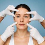 A woman wearing gloves examines her face, highlighting the topic of Botox versus fillers for cosmetic treatments.